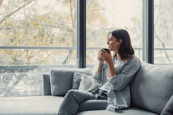 A woman relaxing on the couch with a cup of coffee while the home looks freshly cleaned.